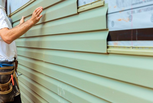 Construction worker carefully aligns, installs green pvc siding board on exterior of house in during renovation project.