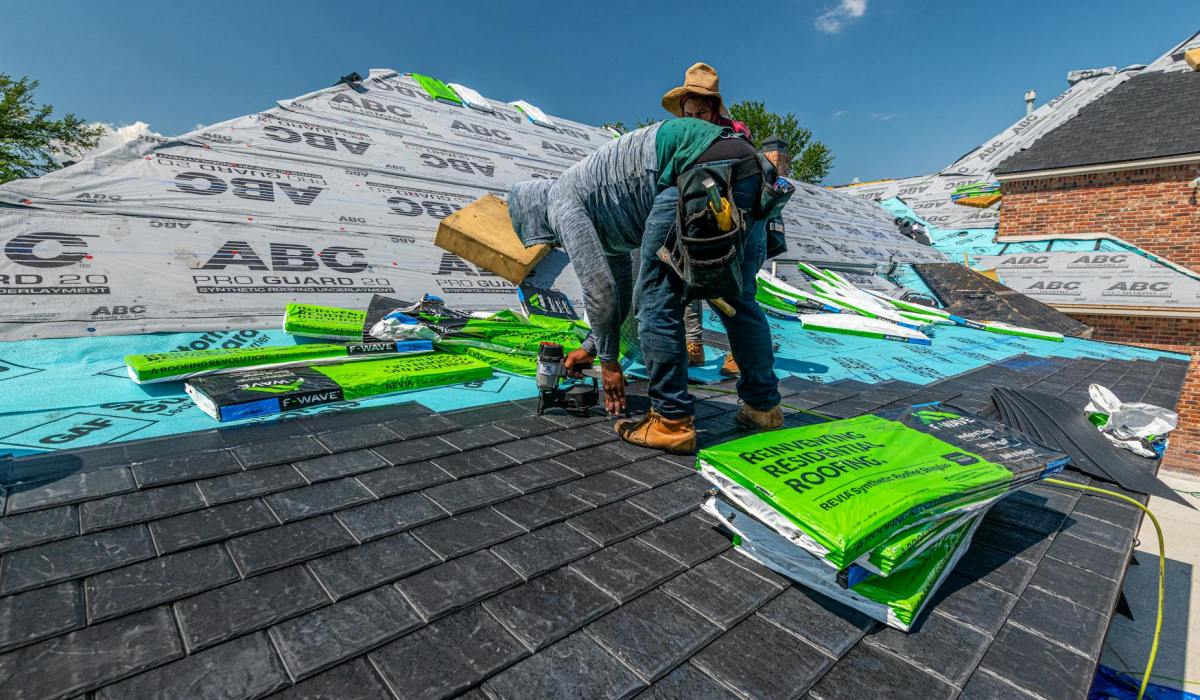 Roofing workers installing synthetic slate roof on brick house during roof repair project